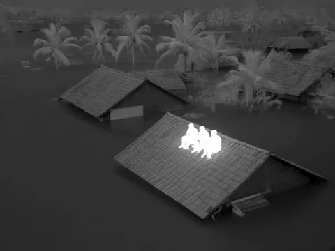 Thermal view: three people on a flooded roof glow white